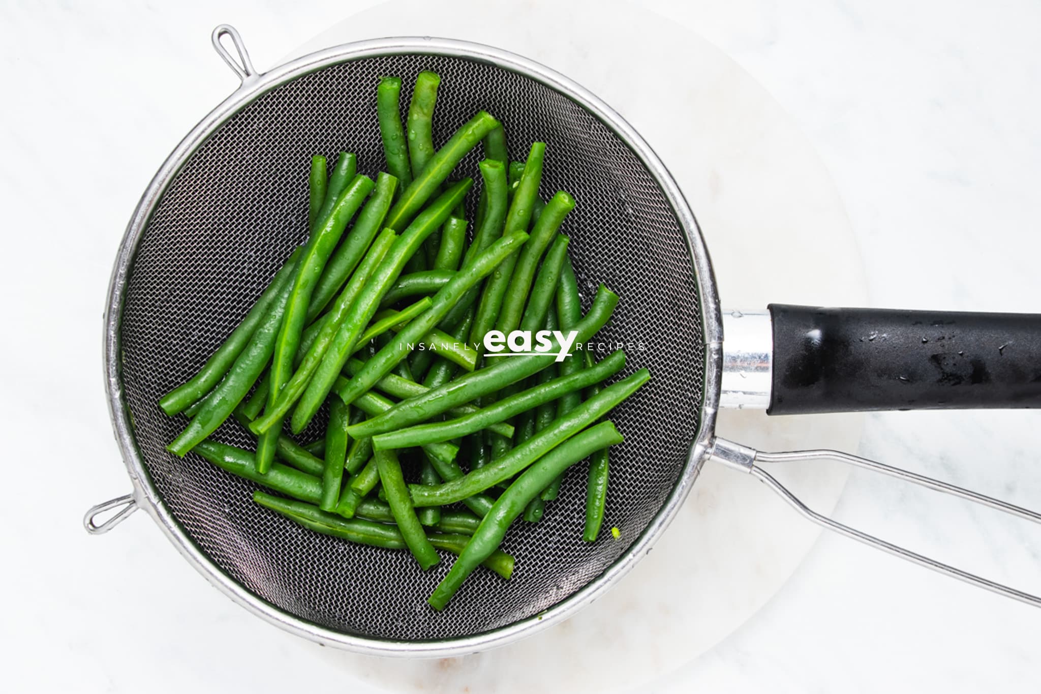 blanched green beans in a mesh strainer, viewed from above.