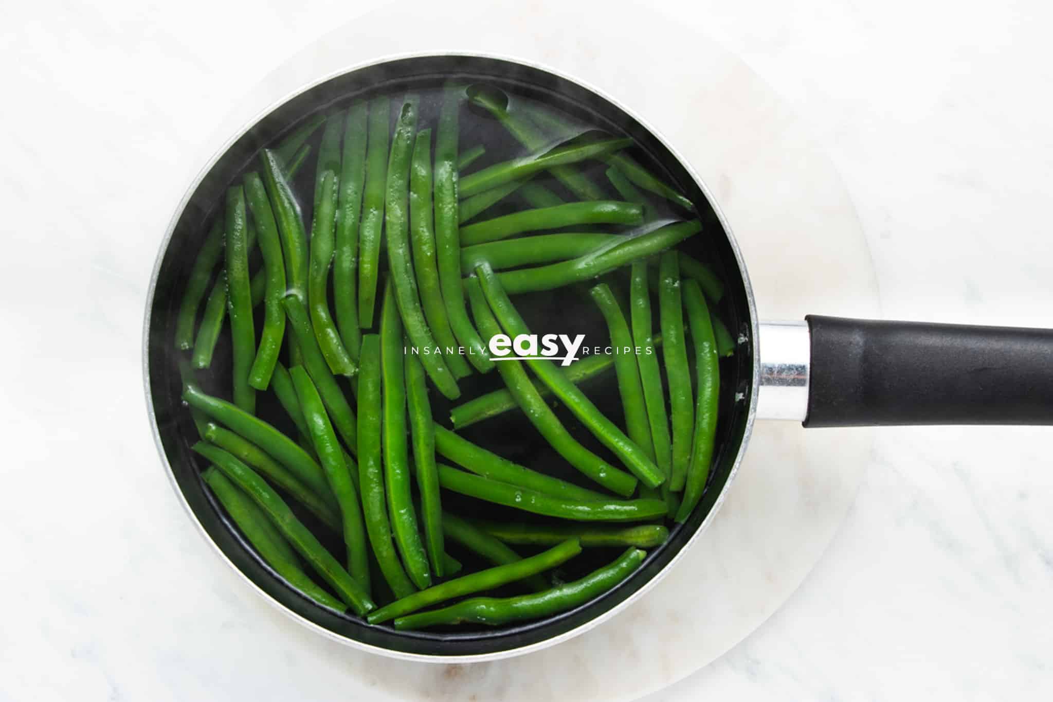 whole fresh green beans in a pot of boiling water, viewed from above.