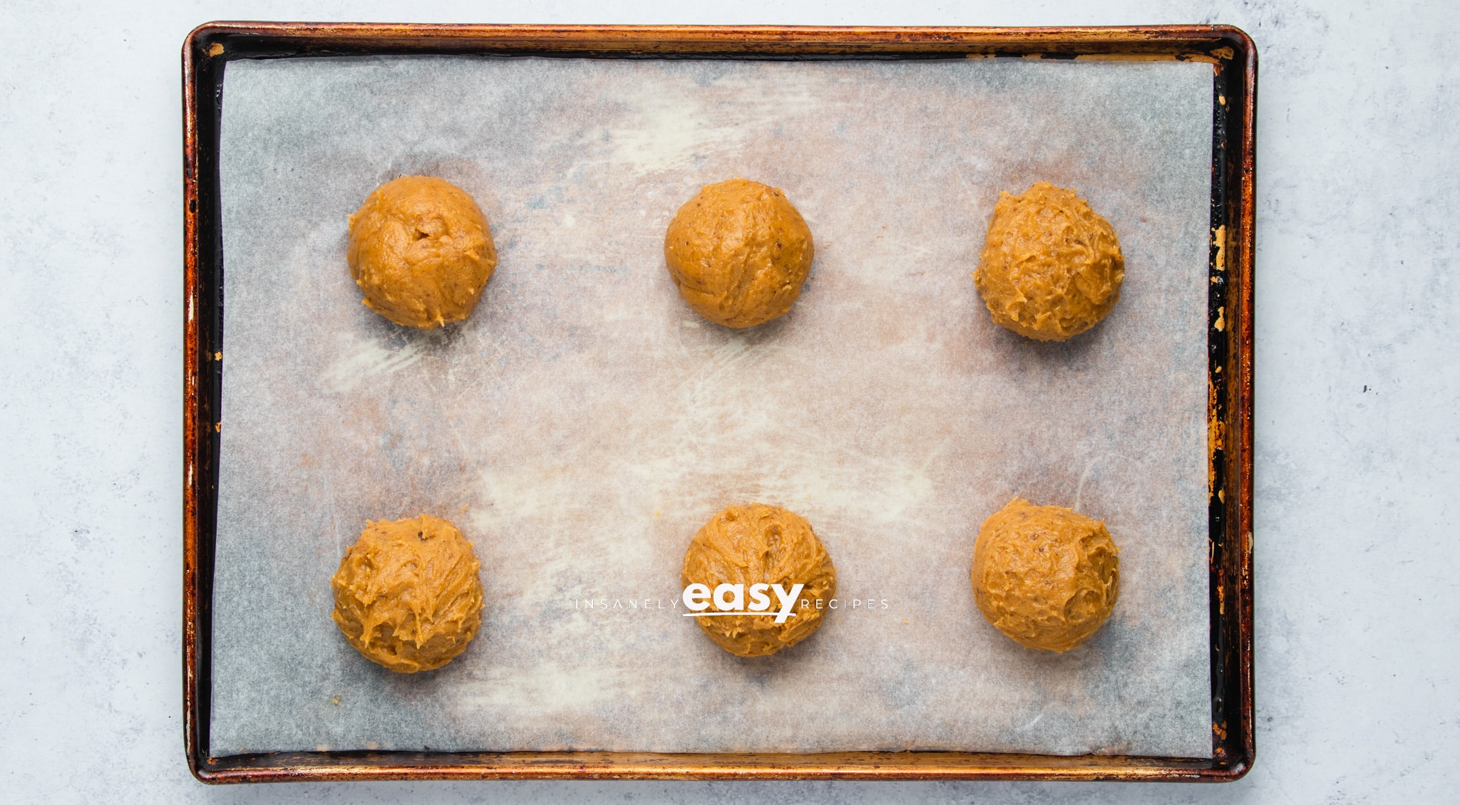 Top view photo of Vegan Pumpkin Cookie dough, formed into six balls, and spread out on a cookie sheet lined with parchment paper.