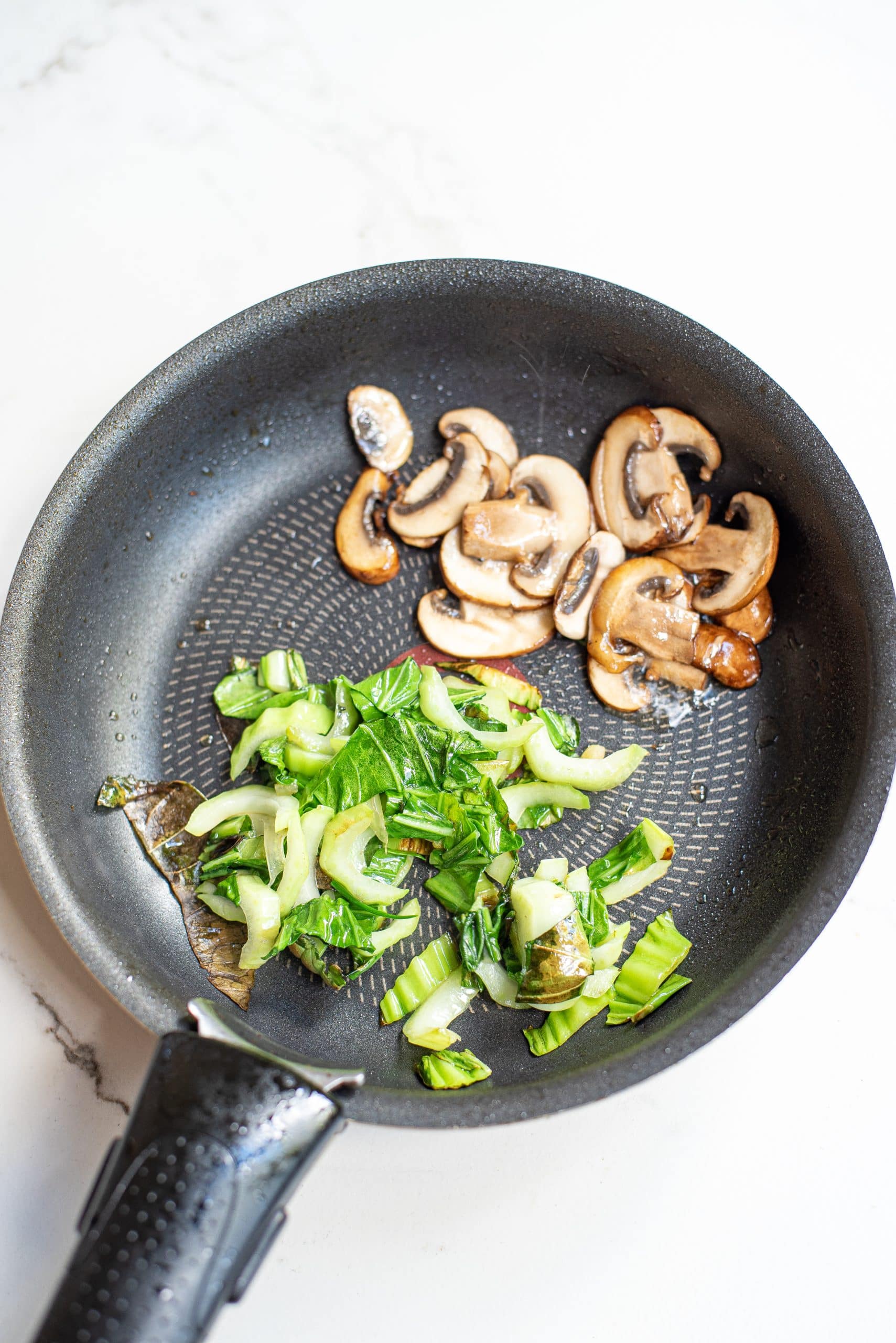 Top view photo of bok choy and mushrrom cooking in a skillet until tender.