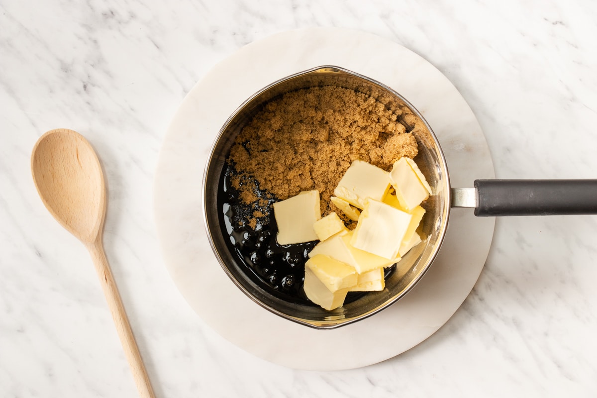 top view photo of vegan butter, sugar, and molasses in a medium saucepan with a wooden spoon to the left.