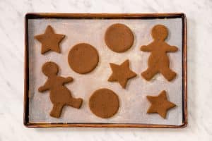 top view photo of vegan gingerbread dough, cut out into gingerbread shapes, on a sheet pan with parchment paper, ready to be baked.