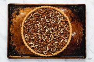 top view photo of pie crust on a baking sheet, with chopped pecans added to the crust