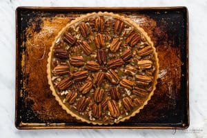 top view photo of pie crust filled with pecans and wet pie mixture, and topped with whole pecans in a decorative manner, on a baking sheet, ready to bake