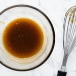 top view photo of brown sugar and melted butter in a clear bowl, whisked together with a whisk next to it