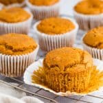 Closeup photo of Vegan Pumpkin Muffins, cooling on a wire rack. There is a kitchen towel in the foreground.