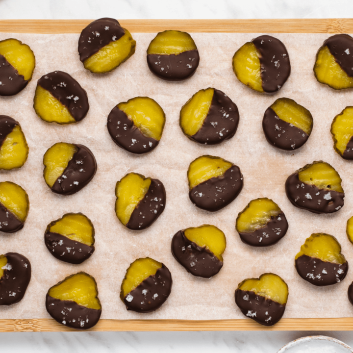 top view photo of pickles dipped in chocolate and sprinkled with salt, on a sheet of parchment paper on a wooden cutting board