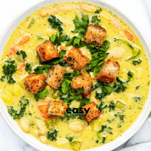 a bowl of creamy soup with white beans and kale, topped with homemade croutons, viewed from directly above.