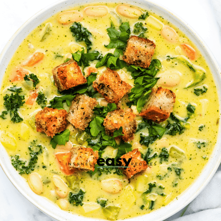 a bowl of creamy soup with white beans and kale, topped with homemade croutons, viewed from directly above.