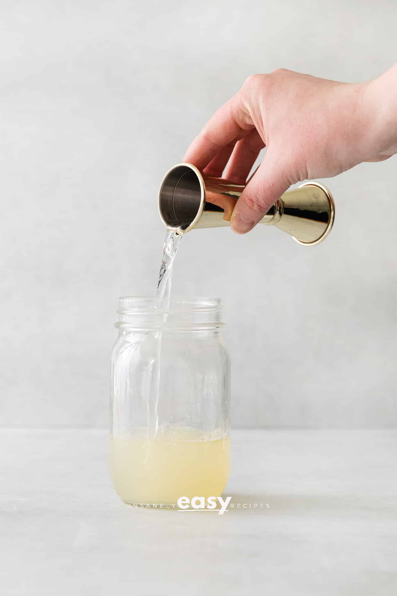 hand pouring yellow liquid into ball jar