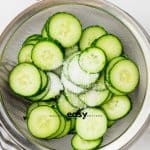 Salted cucumber slices in a mesh sieve, draining.