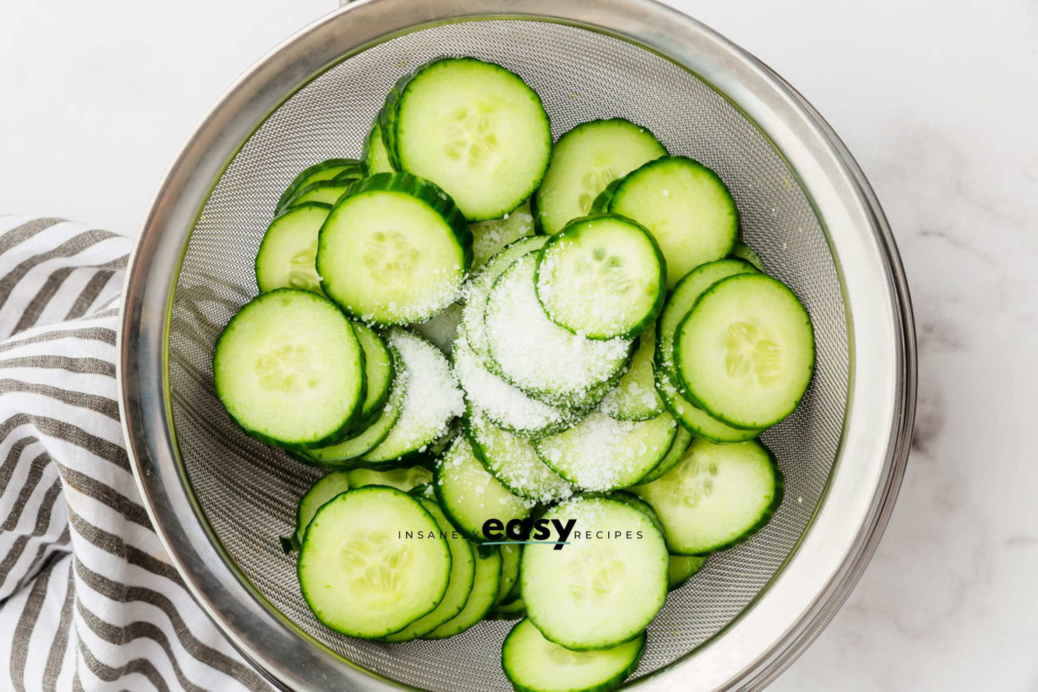 Salted cucumber slices in a mesh sieve, draining.