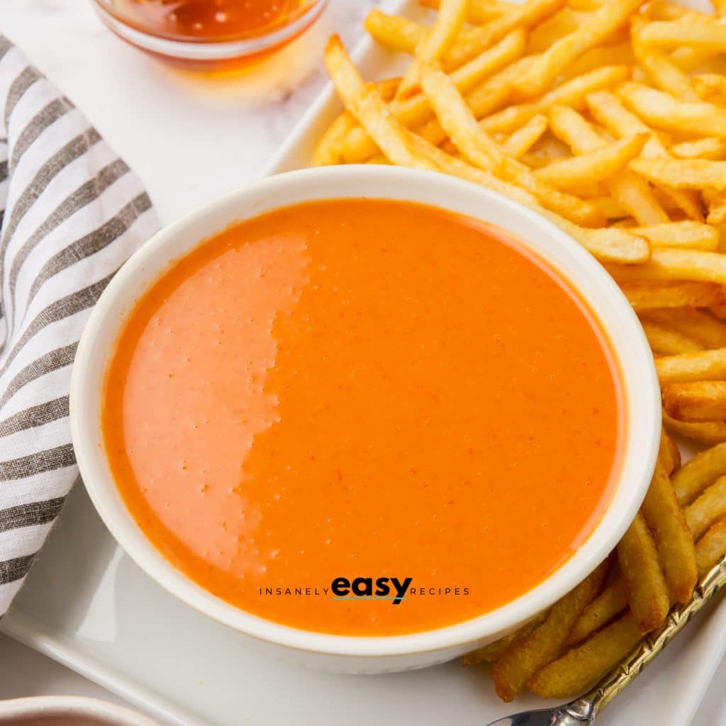 orange sauce in white bowl surrounded by fries