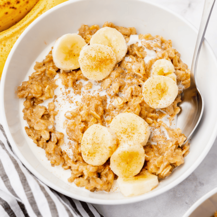 Photo of a white bowl with Bananas and Cream Oatmeal in it. There is a silver spoon in the bowl.