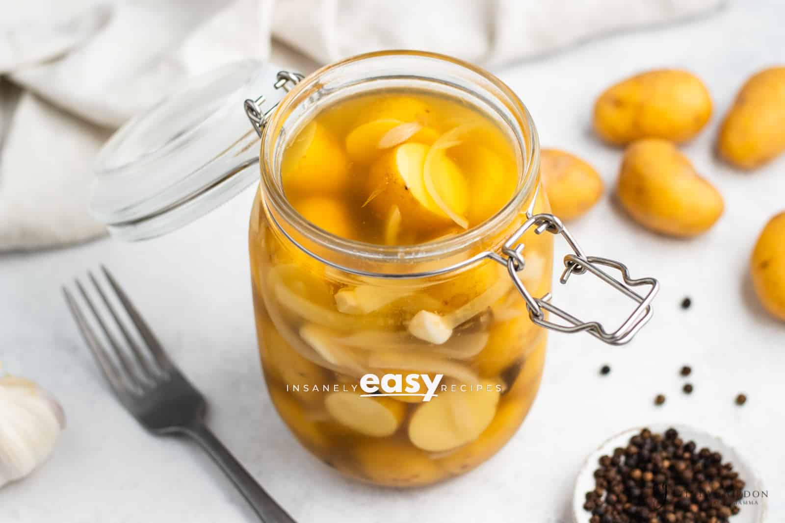 clear glass jar with yellow baby round potatoes cut in half with thin white onion slices in milky liquid.