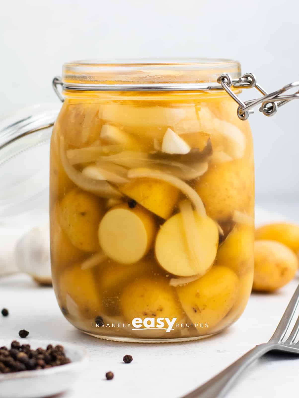 clear glass jar with yellow baby round potatoes cut in half with thin white onion slices in milky liquid. 