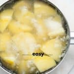 Top view photo of a saucepan with cubed potatoes covered in water and boiling.