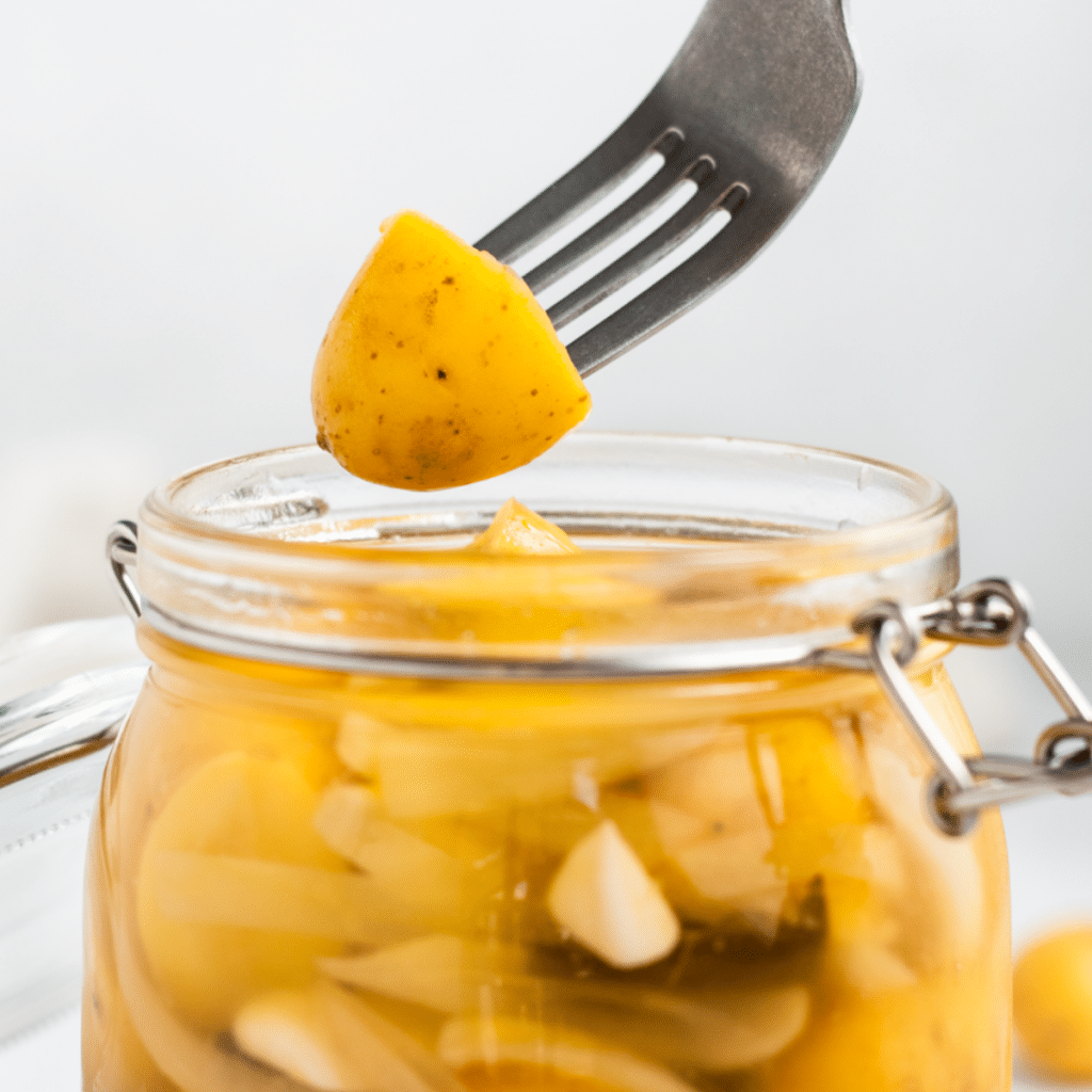a fork holding up a piece of pickled potato above a glass jar