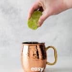 Photo of lime juice being squeezed into a cooper mug.