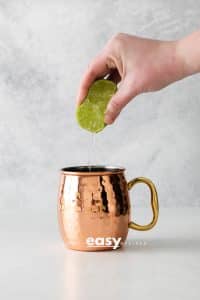 Photo of lime juice being squeezed into a cooper mug.