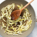 thin white onion slices in saute pan with wooden spoon