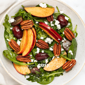 a green salad with apples, grapes, pecans, and feta cheese, on a plate, next to a fork.
