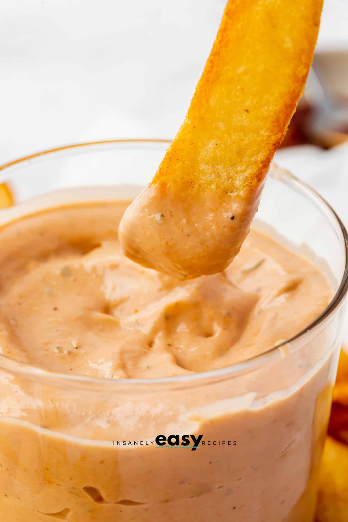 Closeup photo of a french fry, being dipped in a small glass bowl filled with BBQ Ranch. 
