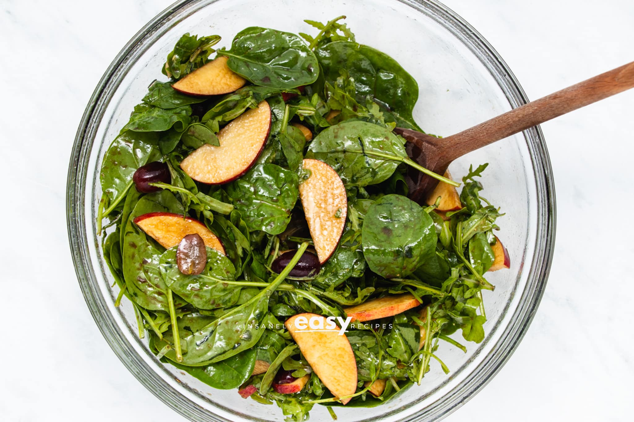 Apple pecan salad tossed with arugula and baby spinach in a mixing bowl.