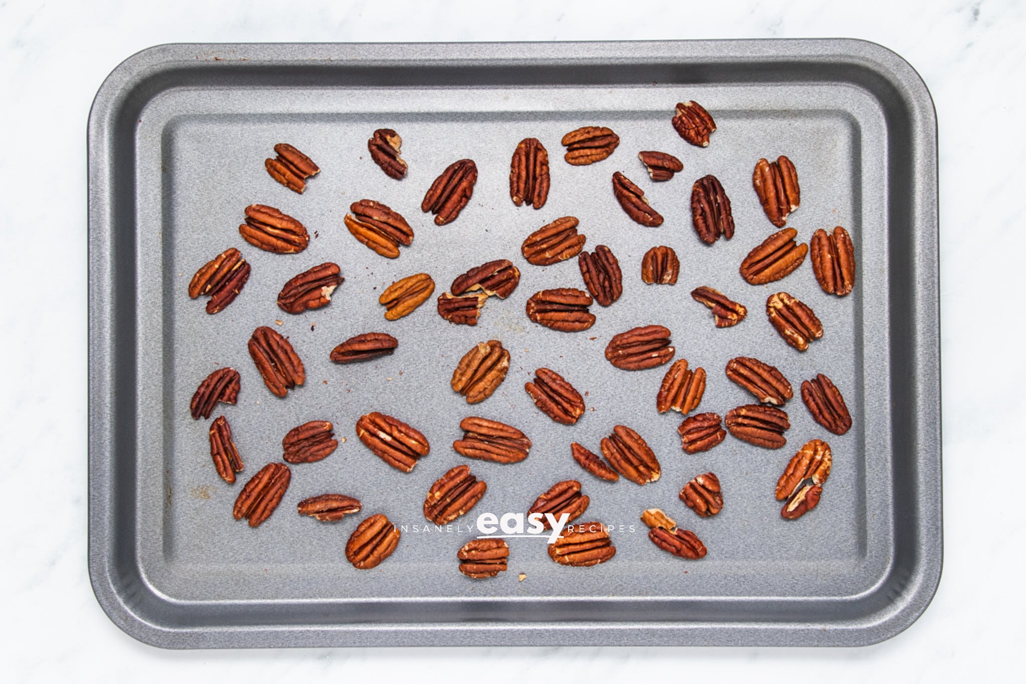 Pecan halves spread out on a baking sheet for toasting.