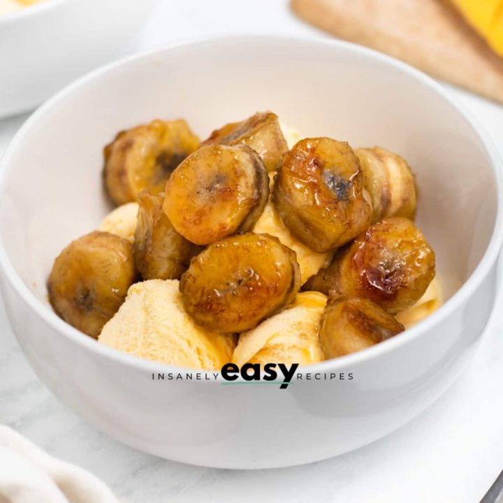 Closeup photo of caramelized bananas on vanilla ice cream in a white bowl.