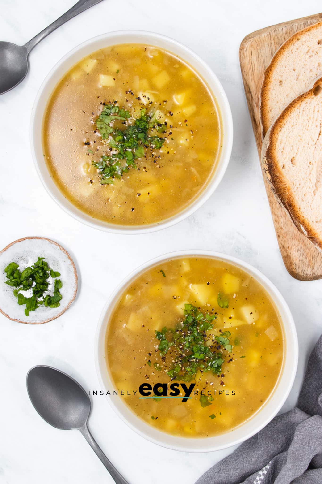 two bowls of simple 3 ingredient potato soup on a table next to a stack of sliced bread.