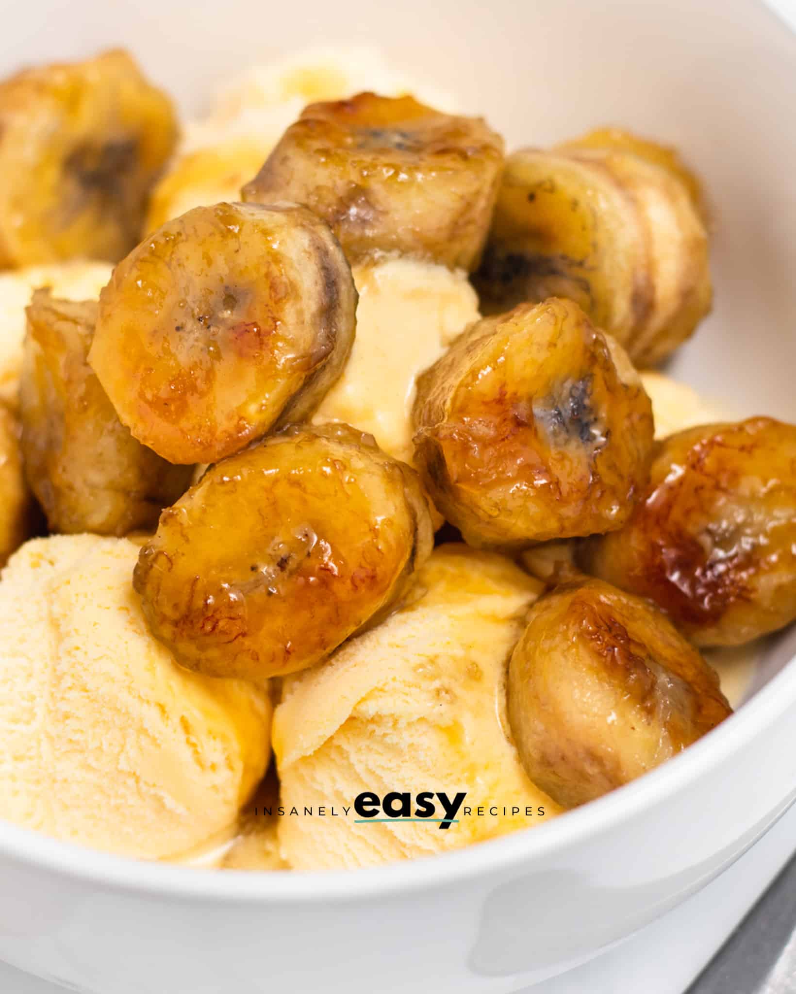 Closeup photo of caramelized bananas on vanilla ice cream in  a white bowl. 