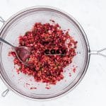 Top view photo of a sieve with cranberry mixture in it, allowing it to drain of excess liquid.