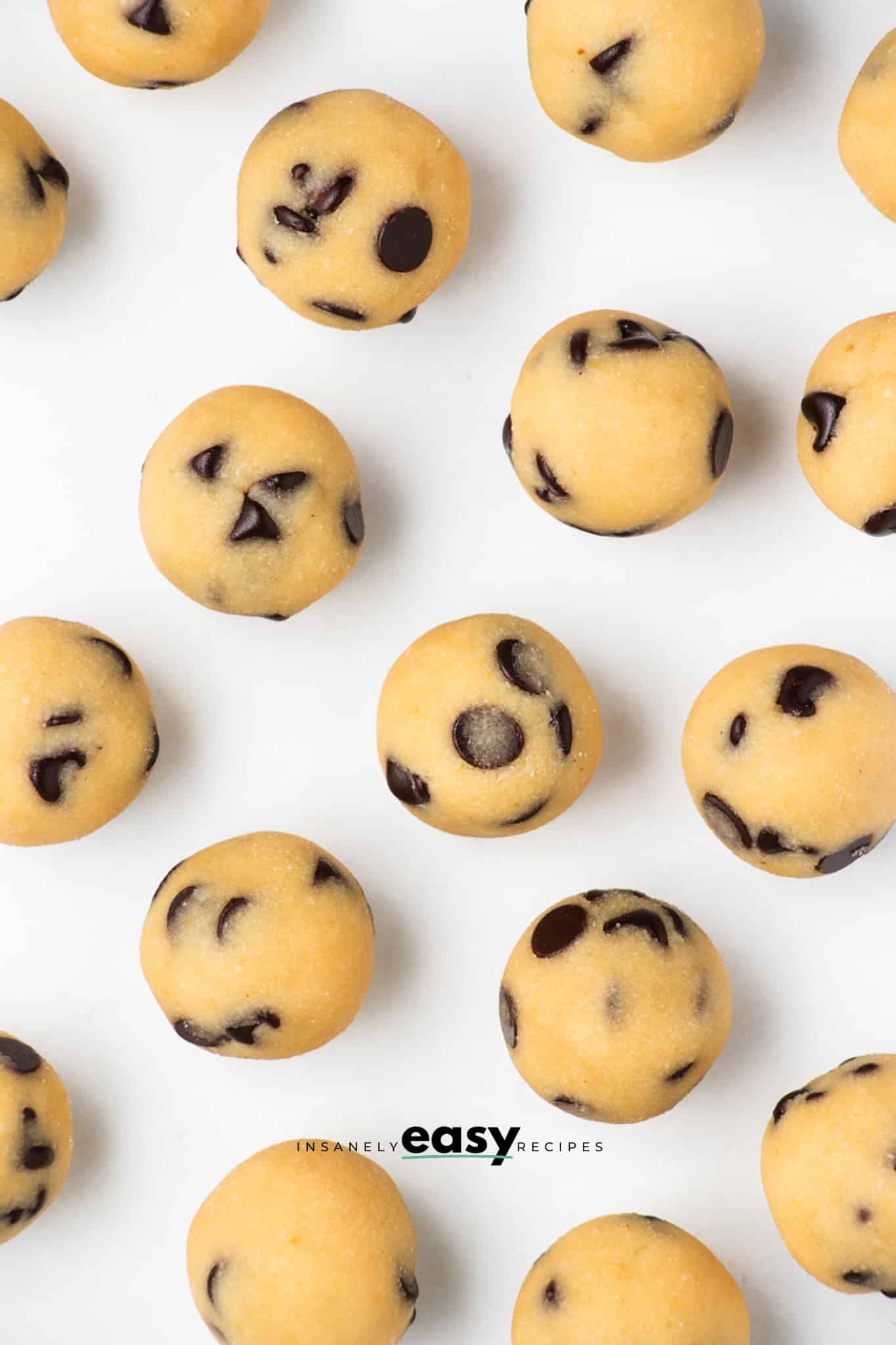Top view photo of cookie dough bites on a white countertop, spread out over the countertop. 