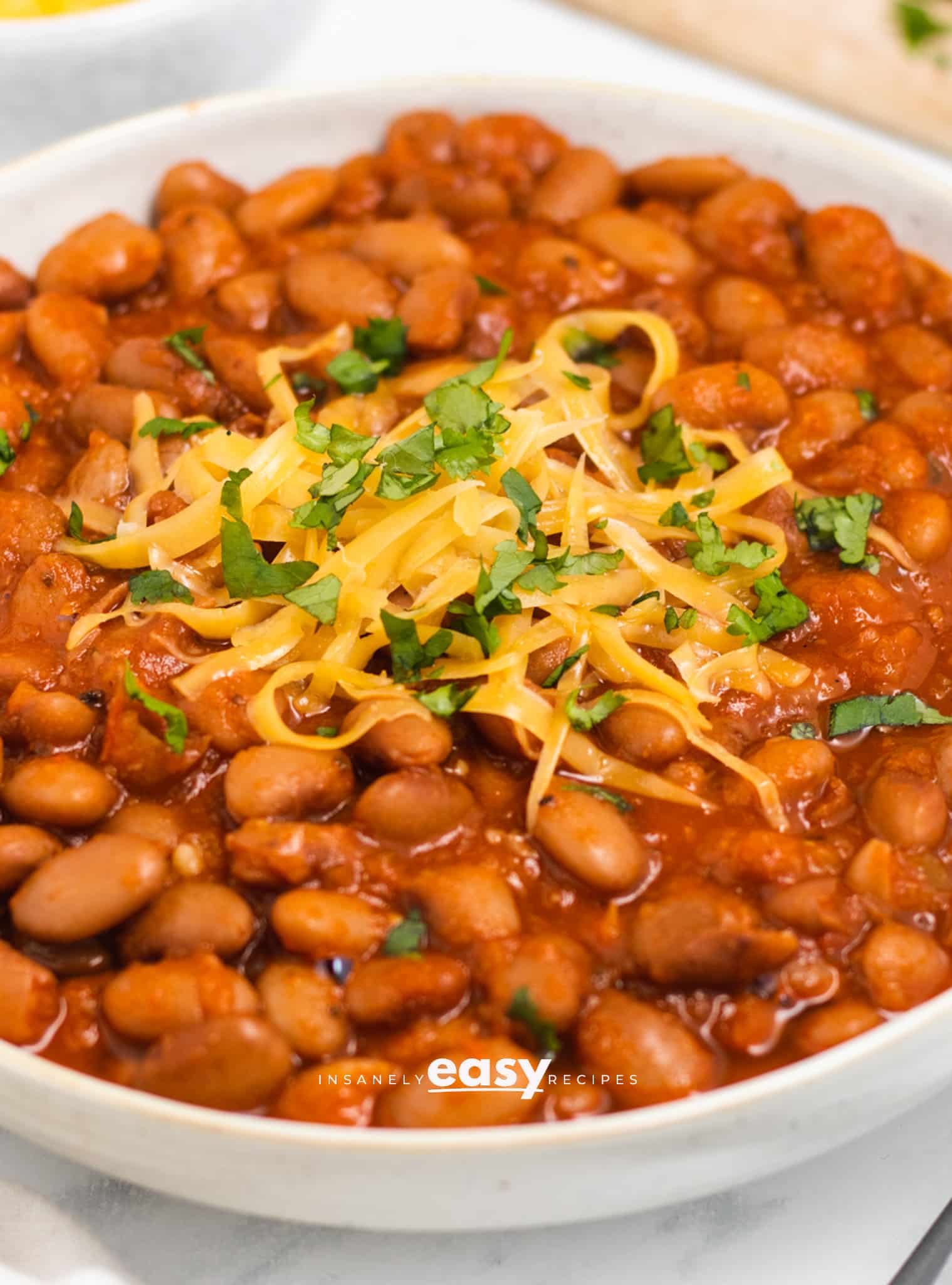 a bowl filled to the top with seasoned ranch style beans. They are topped with shredded cheese and herbs. 