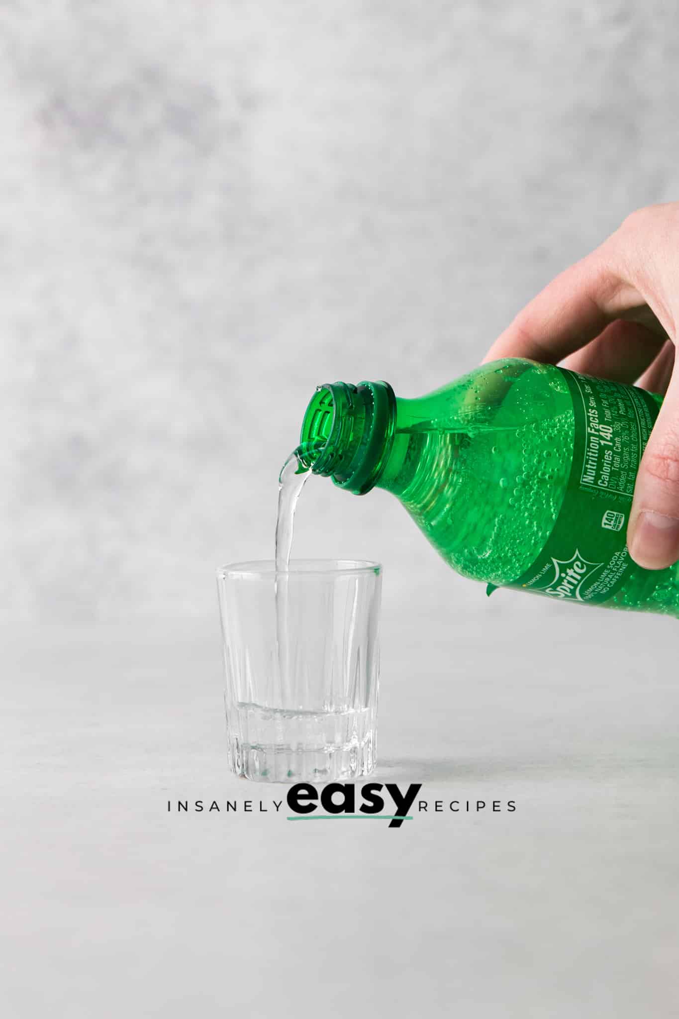 Photo of a hand pouring lemon-lime soda into a shot glass.