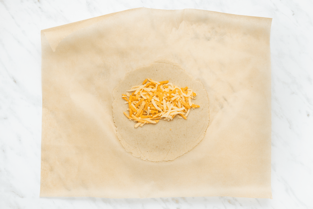 cheese on a tortilla that is on a piece of parchment paper.