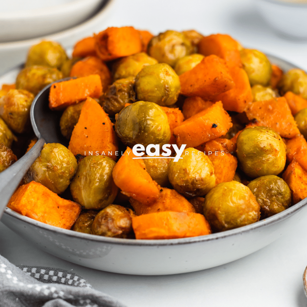 Photo of a white bowl filled with roasted brussel sprouts and sweet potatoes, ready to enjoy.