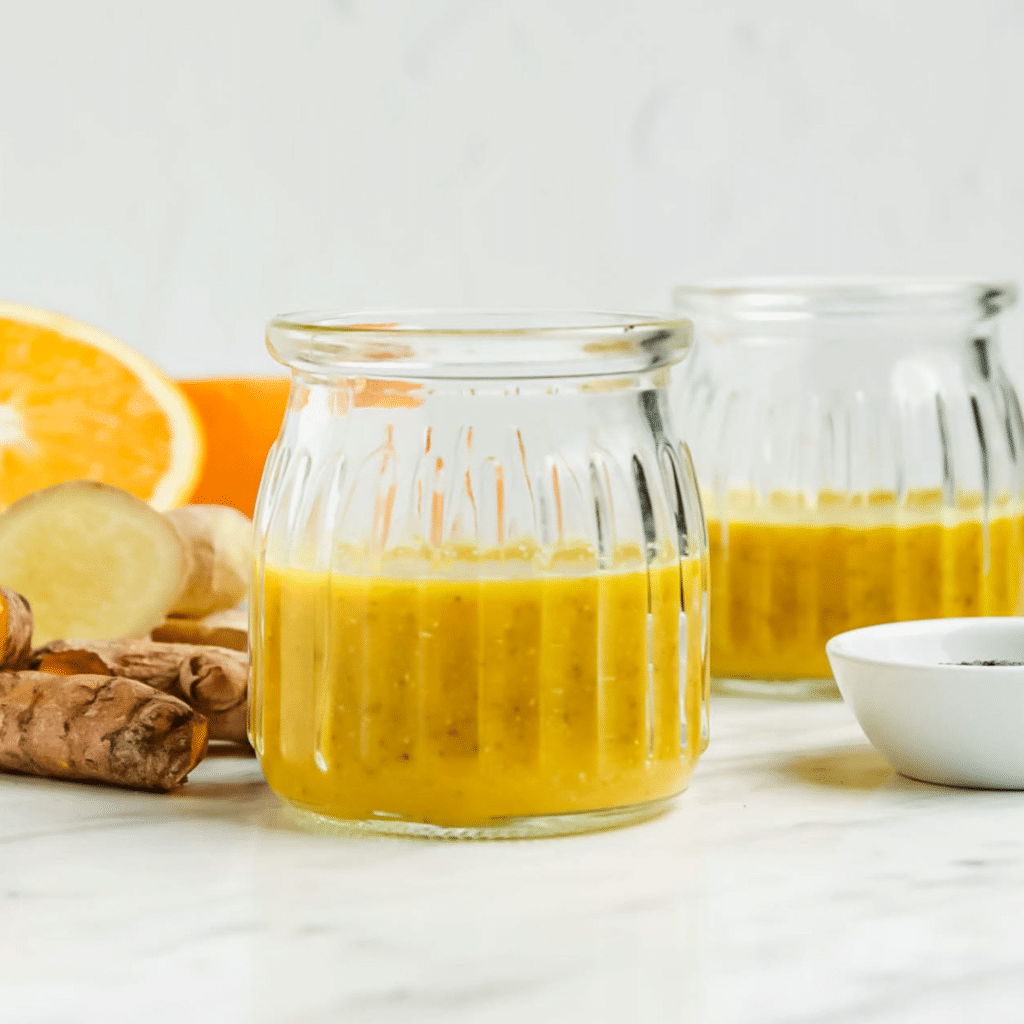 Closeup photo of a Wellness Shot, consisting of orange juice, fresh turmeric, and chia seeds, in a small glass cup.