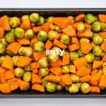 Top view photo of brussel sprouts and sweet potato chunks on a sheet pan, ready to roast in the oven.