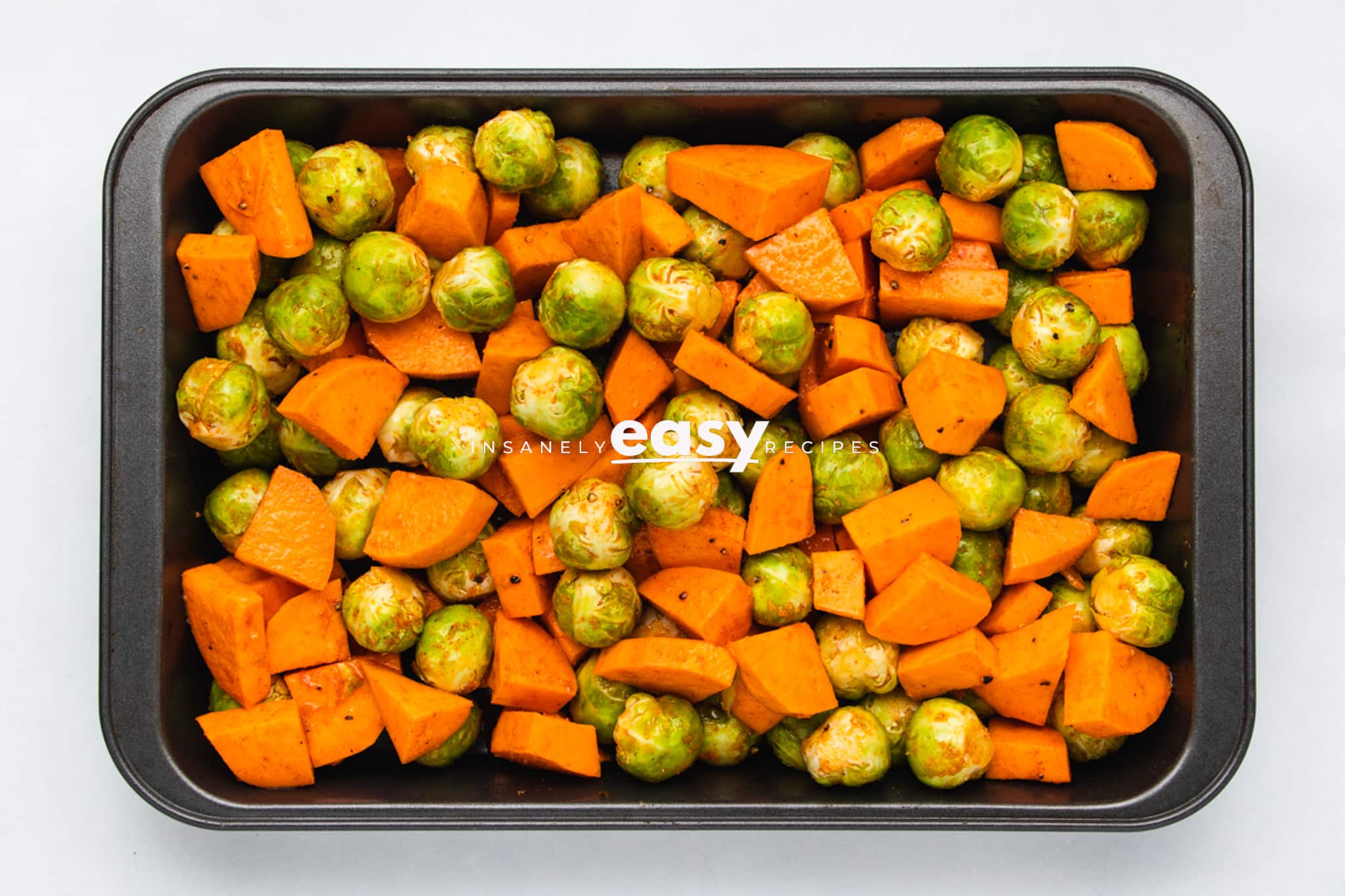 Top view photo of brussel sprouts and sweet potato chunks on a sheet pan, ready to roast in the oven.