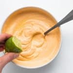 A hand squeezes half a lime into a bowl of seasoned sour cream.