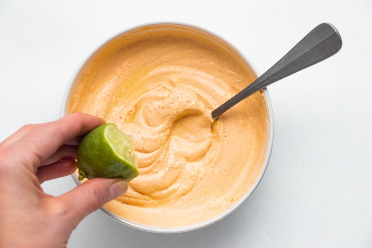 A hand squeezes half a lime into a bowl of seasoned sour cream.