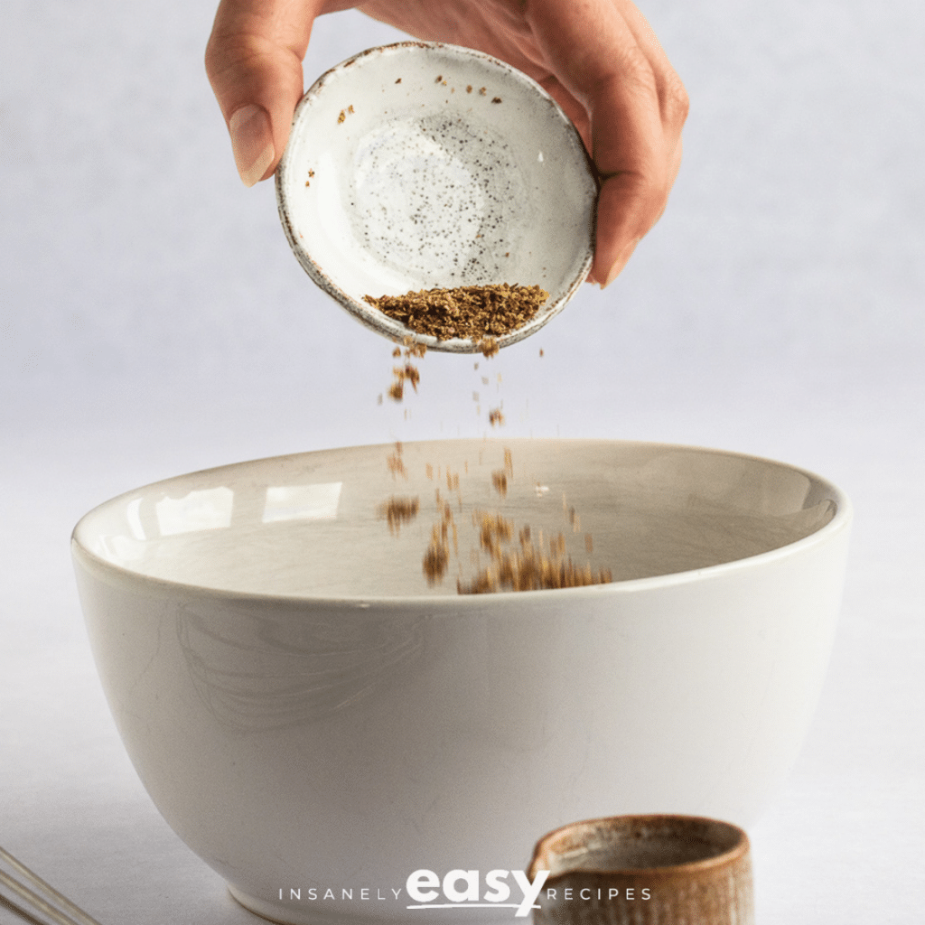 Photo of a hand pouring ground flax seeds into a white bowl.