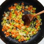 Top view photo of a stockpot with carrots, onions, and celery in the pan and cooking until tender.