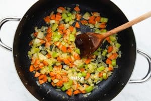 Top view photo of a stockpot with carrots, onions, and celery in the pan and cooking until tender.