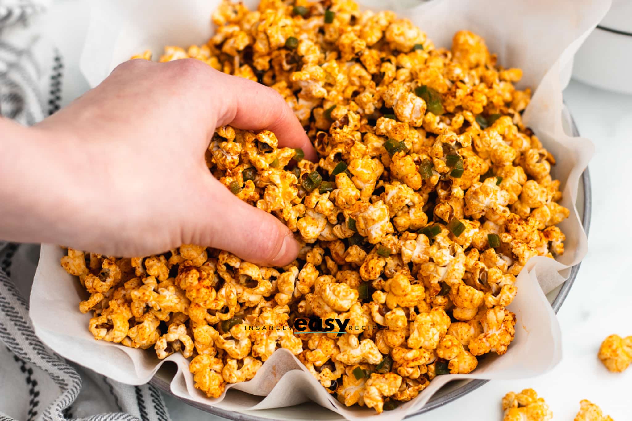 a hand grabbing a handful of jalapeno popcorn from a large bowl. 