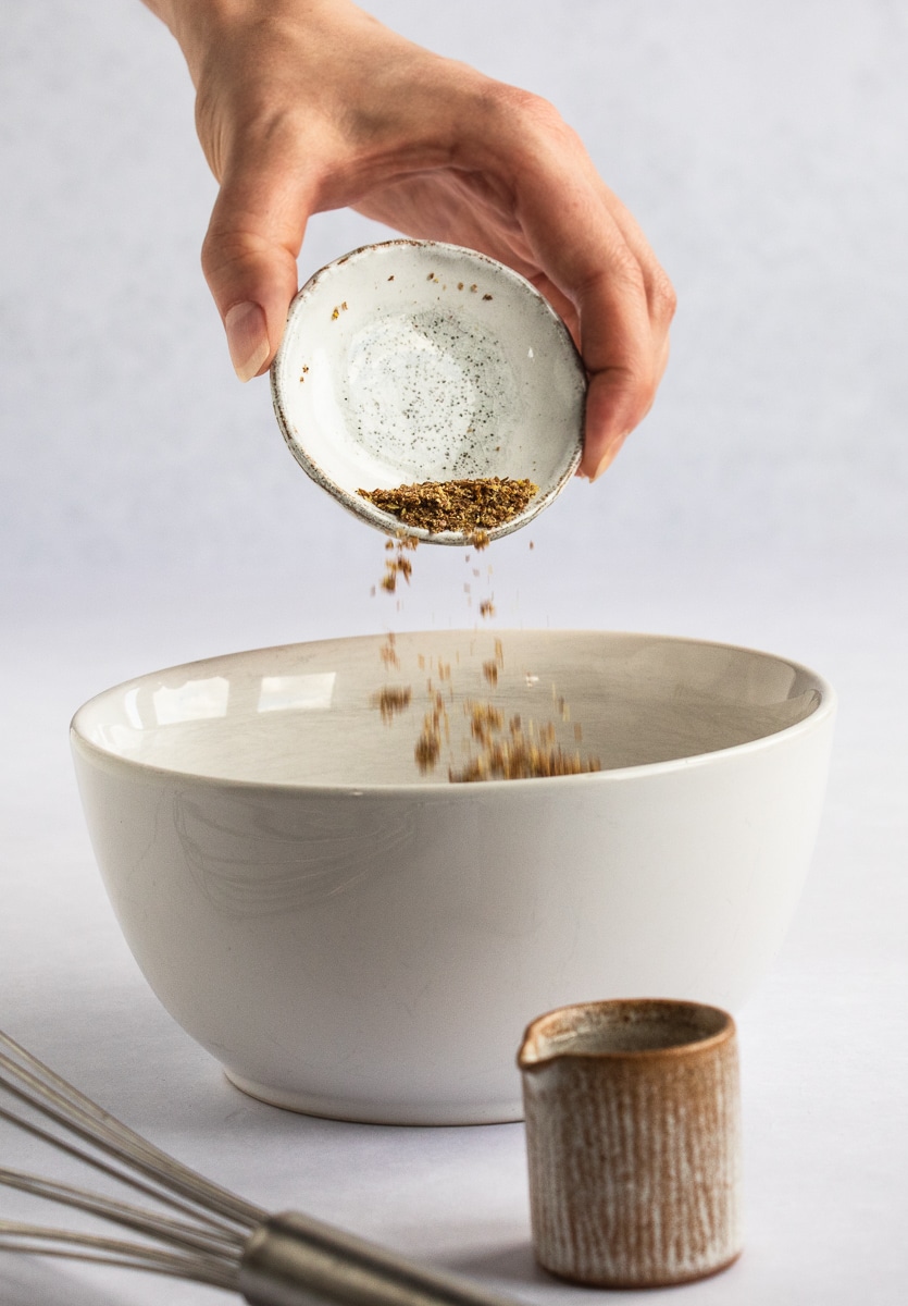 Photo of a hand pouring ground flax seeds into a white bowl.