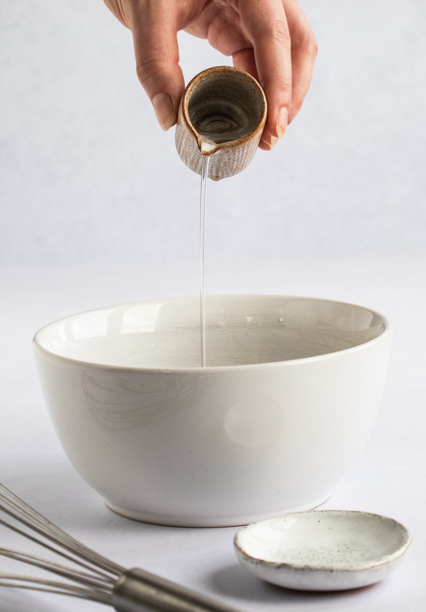 Photo of a hand pouring water into a white bowl with the ground flaxseeds.