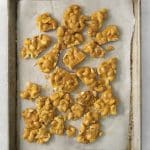 cashew brittle broken up into pieces on a parchment lined baking sheet